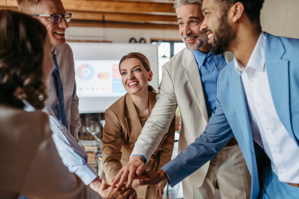 Happy business team stacking hands together to cheer up as they laugh and celebrating their success. Diversity in team work.