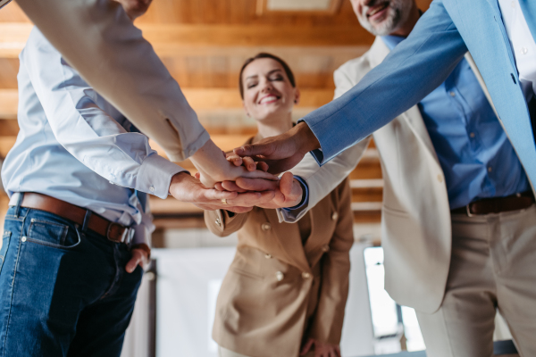 Close up of young colleagues holding hands together, symbol of success and cooperation.