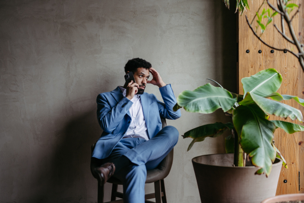 Portrait of a young businessman sitting near window in green office full of plants.