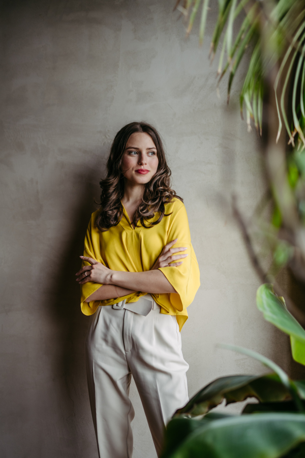 Portrait of a young woman standying near window in room full of plants. Half length portrait of beautiful caucasian female manager, ceo, lawyer.