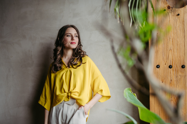 Portrait of a young woman standying near window in green office full of plants.