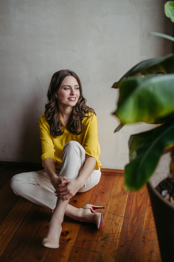 Portrait of a young woman sitting near window in room full of plants. Full length portrait of beautiful caucasian female entrepreneur.