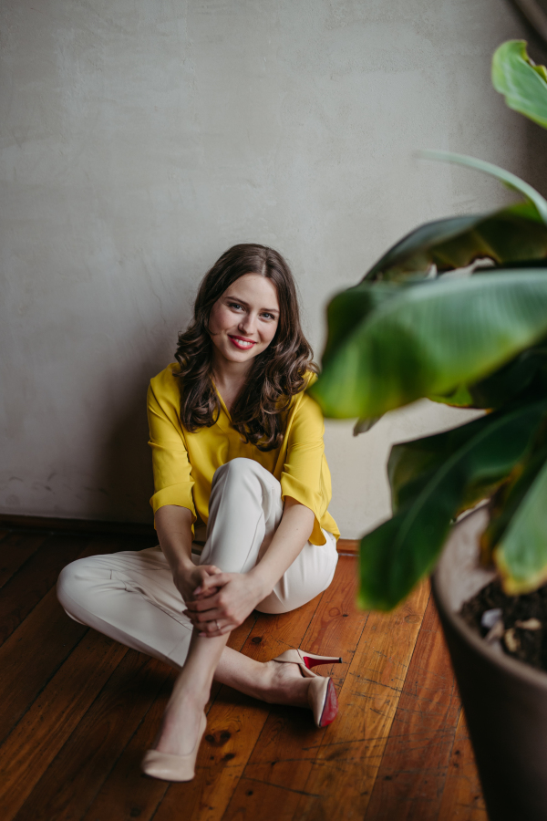 Portrait of a young woman sitting near window in green office full of plants.