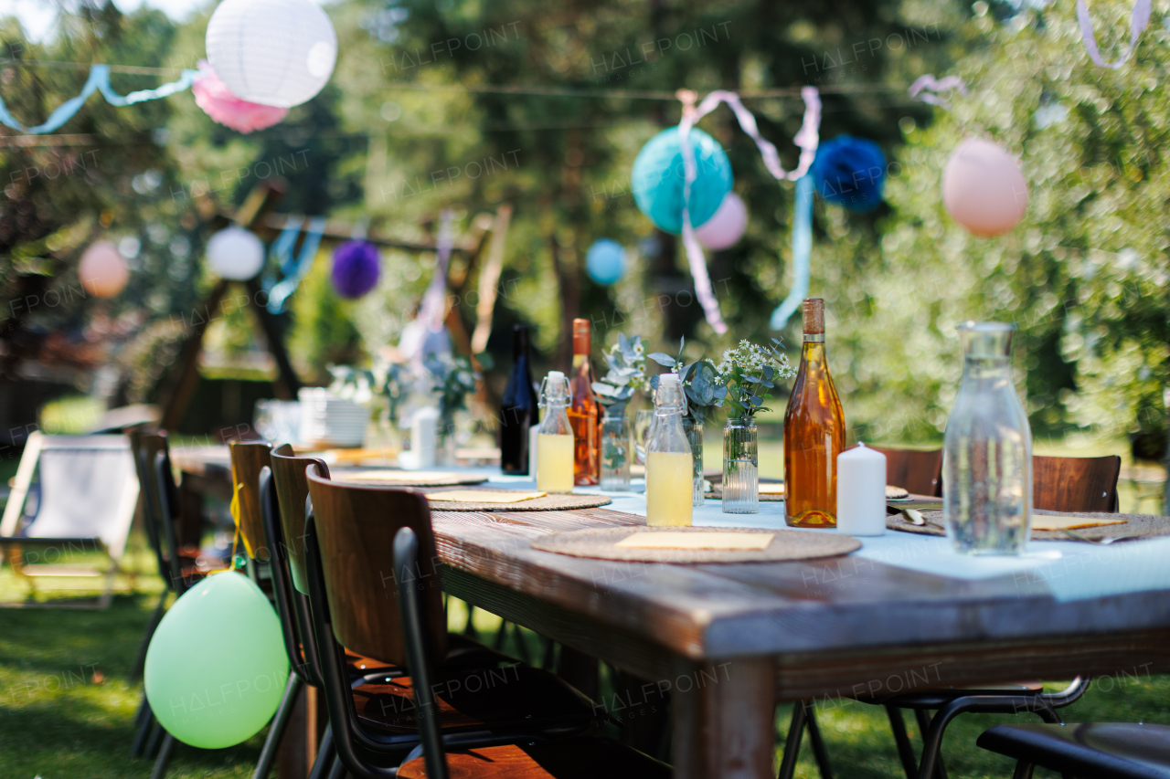 Close up shot of a set table at a summer garden party. Table setting with glasses, fruit lemonade, fresh fruits and salads and delicate floral decoration. Colorful paper decorations for party.