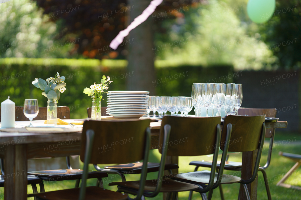 Close up shot of set table at summer garden party, empty plates and glasses. Table setting with glasses, lemonade, delicate floral and paper decoration.