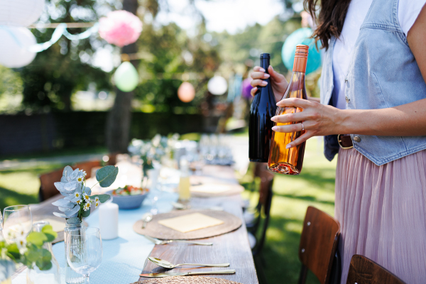 Young beautiful woman preparing refreshments for a summer garden party. The hostess is holding bottles of wine.