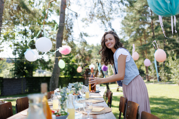 Young beautiful woman preparing refreshments for a summer garden party. The hostess is holding bottles of wine.