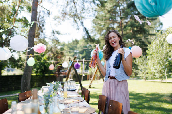 Young beautiful woman preparing refreshments for a summer garden party. The hostess is holding bottles of wine.