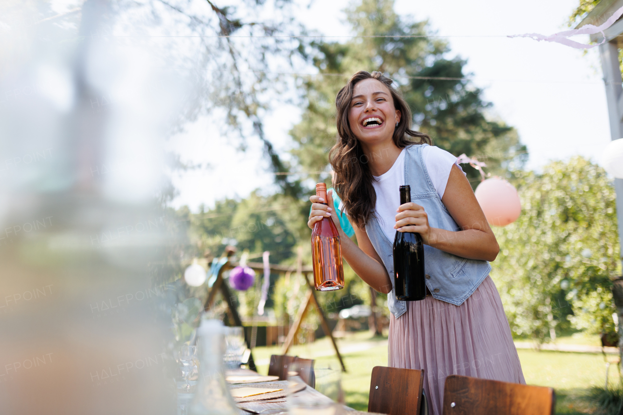 Young beautiful woman preparing drinks for a summer garden party. The hostess is holding bottles of wine.