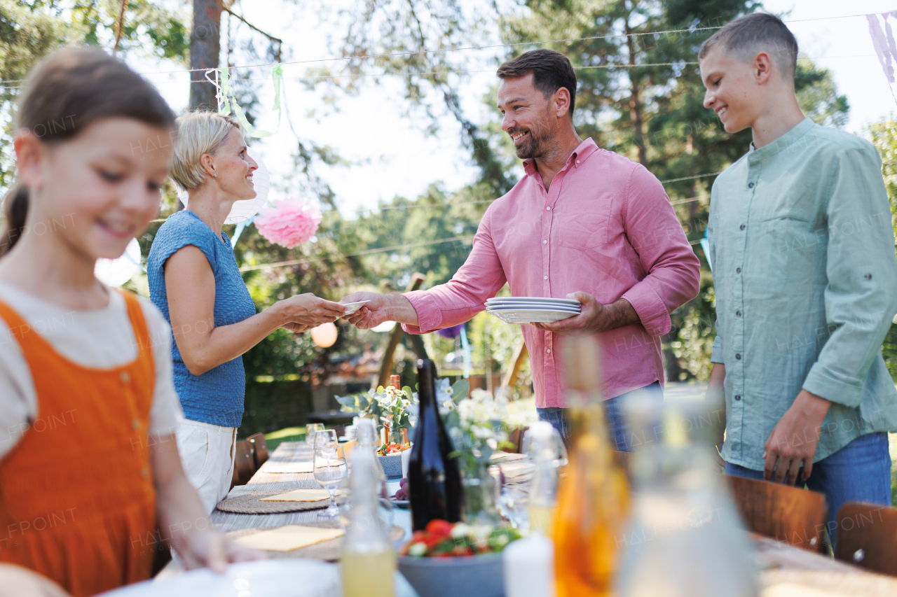 Family setting table for summer garden party. Bringing plates, food, and drinks.