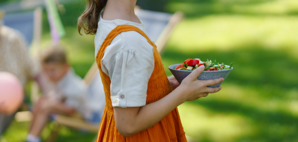 Close up of young girl setting table for summer garden party. Girl holding plate with fresh vegetable salad. Summer garden banner with copy space. Getting ready for family gathering.