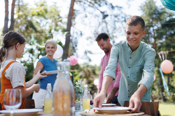 Family setting table for summer garden party. Bringing plates, food, and drinks.