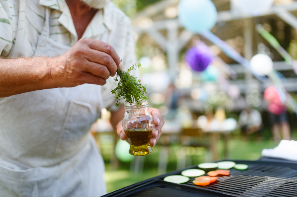 Close up of a man grilling at a bbq garden party. Chef using herbs to brush food with oil. Grilled vegetables.