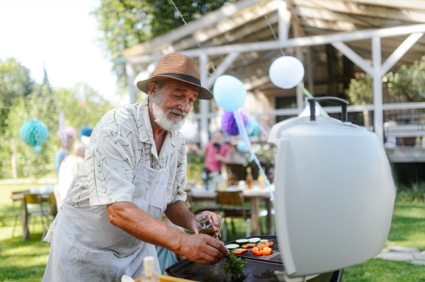 Close up of a senior man grilling at a bbq garden party. Elderly Chef using herbs to brush food with oil. Grilled vegetables.