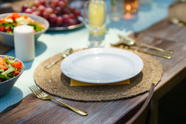 Close up shot of a set table at a summer garden party. Table setting with glasses, lemonade, fresh fruits and salad and delicate floral decoration.