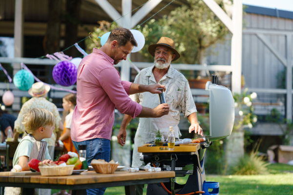 Young boy cutting vegetables for grilling. Father, grandfather and son grilling together at a garden bbq party. Three generations of men at summer family garden party.