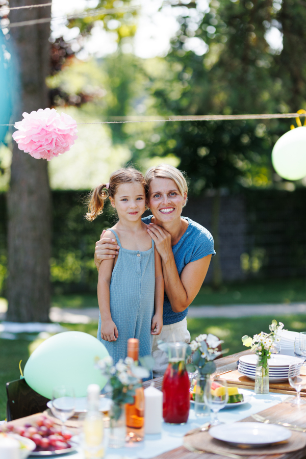 Family portrait at outdoor summer garden party. Aunt with niece standing by table with food and posing for photo.