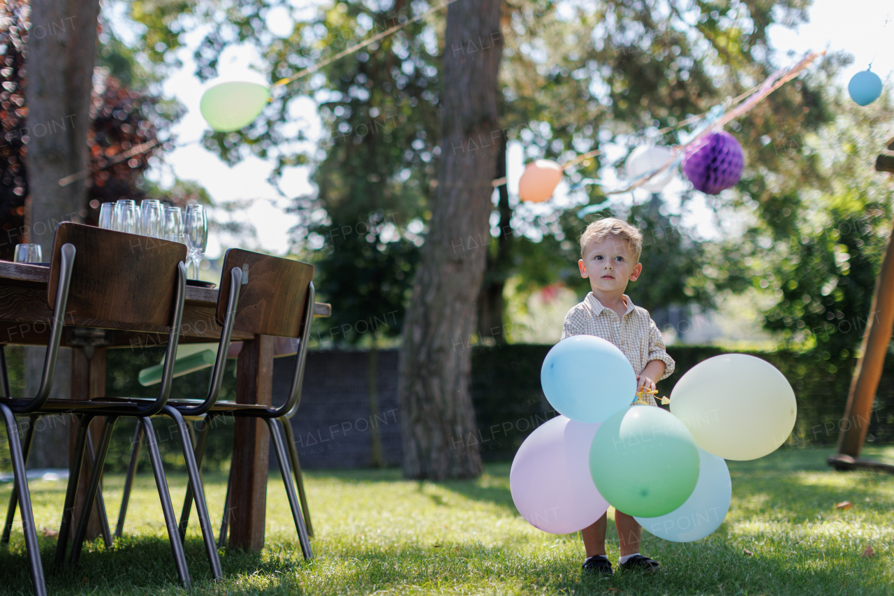 Little boy holding colorful balloons at birthday party outdoors. Birthday garden party for children.