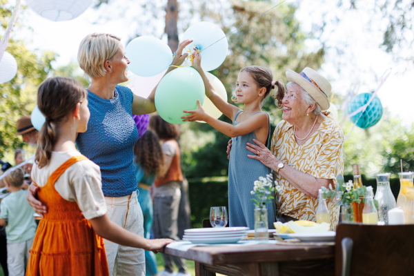 Grandmother, mother and daughter setting decorations for summer garden party. Three generations of women in family, arranging balloons, lanterns and decors. Getting ready for family gathering.