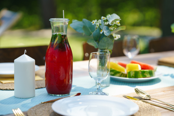 Close up shot of a set table at a summer garden party. Table setting with glasses, fruit lemonade, fresh fruits and salad and delicate floral decoration.