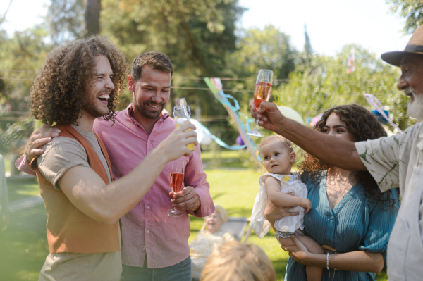 Family toasting and clinking glasses at summer garden party. Multigenerational family gathering,