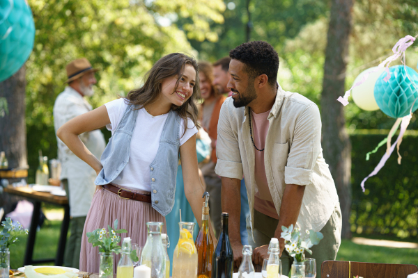 Friends talking, flirting and having fun at a summer grill garden party. Multiracial couple hosting garden party.