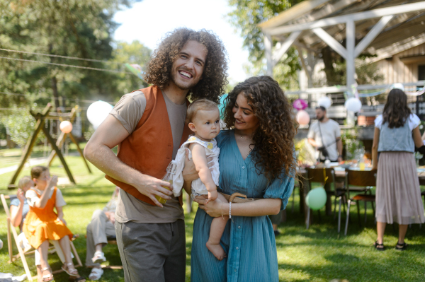 Young parents holding baby at a family garden party. Father, mother, and a small child at birthday party.