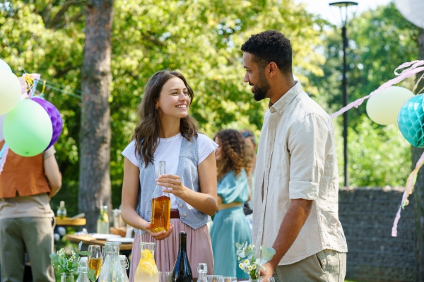 Friends talking and having fun at a summer grill garden party. Multiracial couple hosting garden party.