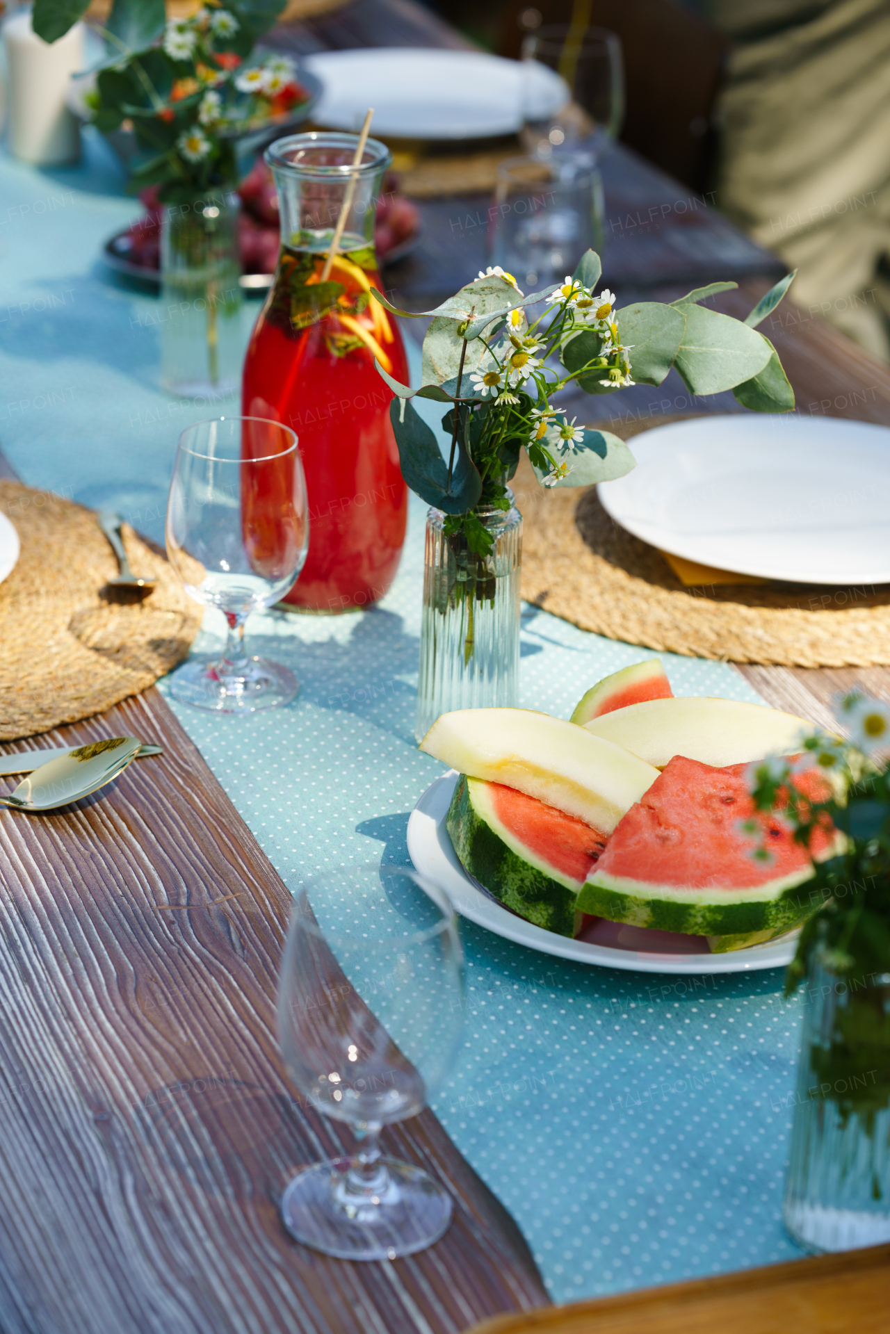 Close up shot of a set table at a summer garden party. Table setting with glasses, lemonade, fresh fruits lemonade and delicate floral decoration.