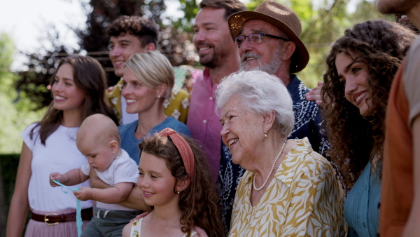 Family video at an outdoor summer garden party. Family and friends standing and posing for a group photo. Multigenerational family.