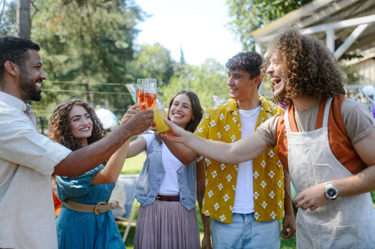 Friends and family raising a toast and clinking glasses at a summer grill garden party. People at the party laughing, holding glasses with drinks.