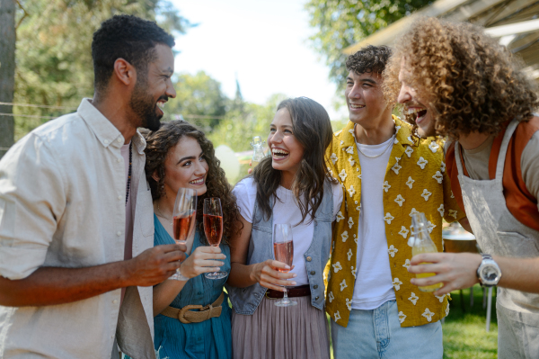 Friends and family talking and having fun at a summer grill garden party. People at the party laughing, holding glasses with drinks.