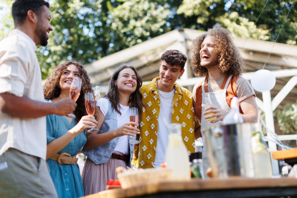 Friends and family talking and having fun at a summer grill garden party. People at the party laughing, holding glasses with drinks.