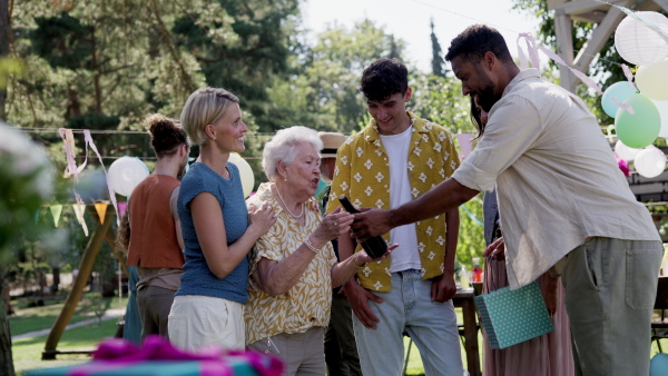 Friends and family talking and having fun at a summer grill garden party. People at the party laughing, holding glasses with drinks.