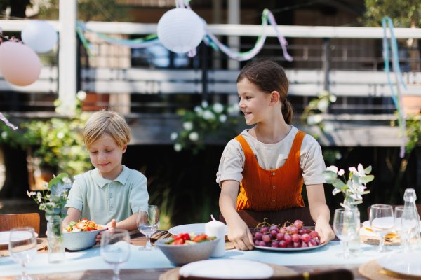 Young kids setting table for summer garden party. Bringing food and drinks on the table.