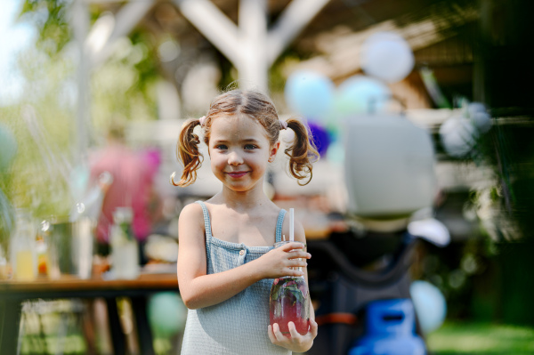 Cute little girl hodling fresh lemonades in glass bottle. Summer garden party at backyard.