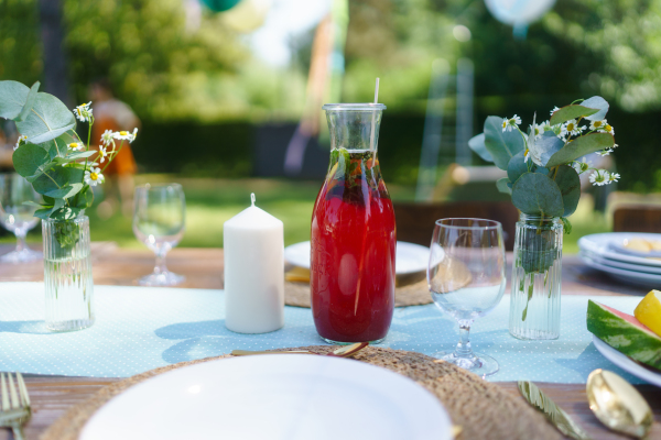 Close up shot of a set table at a summer garden party. Table setting with glasses, fruit lemonade, fresh fruits and salad and delicate floral decoration.