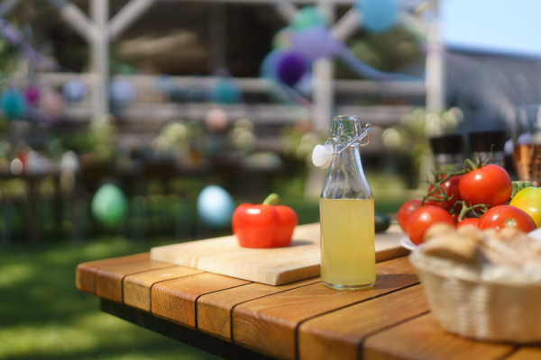 Close up shot of a grill and table at a summer garden party. Side table with wine glasses, lemonade, fresh vegetables and bread.