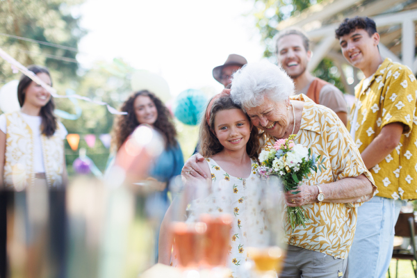 Garden birthday party for senior lady. Beautiful senior birthday woman receiving flowers from granddaughter.