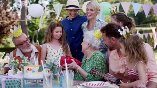 Family birthday garden party. Family sitting at the table having fun, little girl playing ukulele for the birthday man.