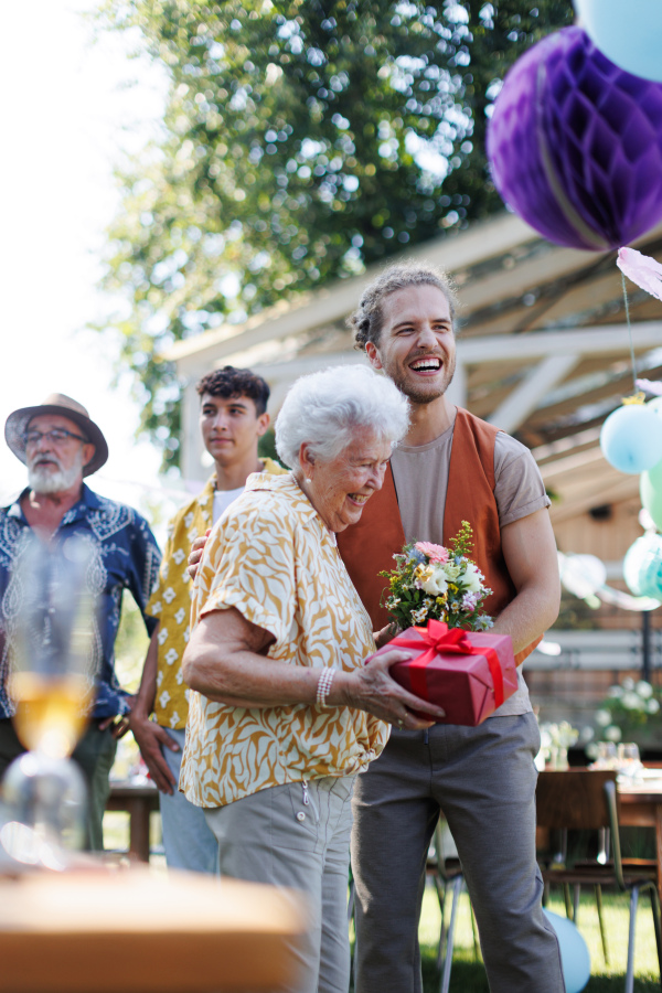 Garden birthday party for senior lady. Beautiful senior birthday woman receiving birthday wishes and gifts from grandson.