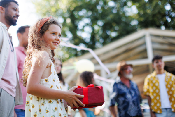 Garden birthday party with surprise. Portrait of geautiful girl holding birthday gift in hands. Family garden gathering during warm autumn day.