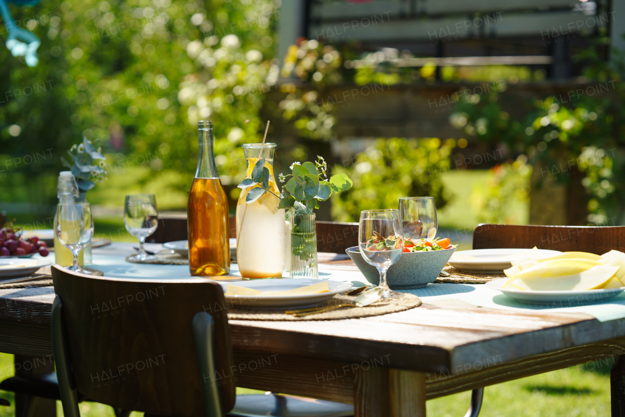 Close up shot of a set table at a summer garden party. Table setting with glasses, lemonade, fresh fruits and salad and delicate floral decoration.