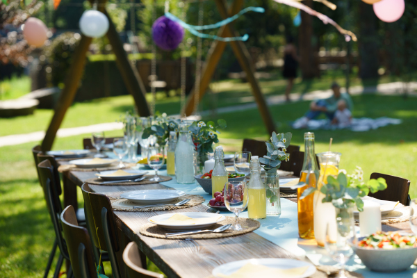 Close up shot of a set table at summer garden party, grilled food. Table setting with glasses, lemonade, delicate floral and paper decoration, and bottles of summer wine.