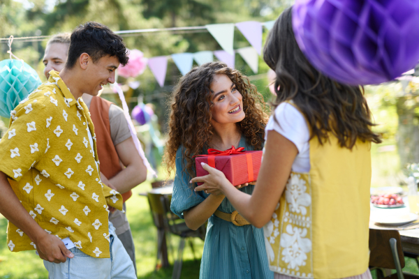 Garden birthday party with surprise for beautiful young woman. Friends holding birthday gifts and flowers.