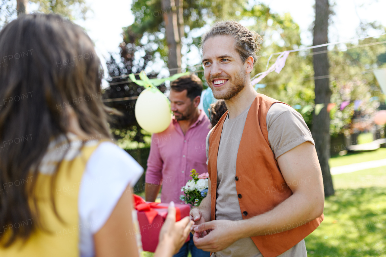 Man gifts a wrapped present to friend as surprise at birthday party. Friends reunite after a long time apart. Man and woman embracing, happy to meet at a garden party.