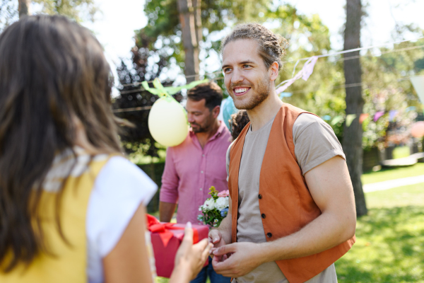 Man gifts a wrapped present to friend as surprise at birthday party. Friends reunite after a long time apart. Man and woman embracing, happy to meet at a garden party.