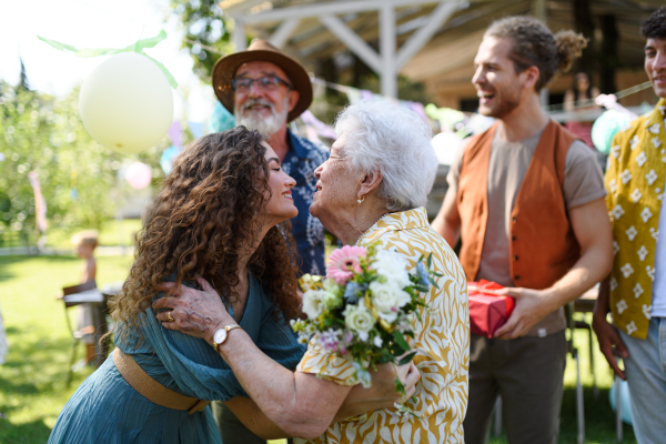 Garden birthday party for senior lady. Beautiful senior birthday woman hugging her granddaughter.