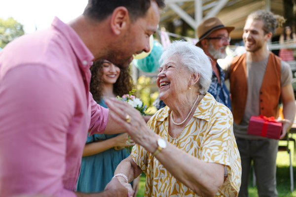 Garden birthday party for senior lady. Beautiful senior birthday woman receiving birthday wishes and gifts.