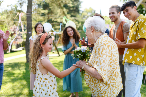 Garden birthday party for senior lady. Beautiful senior birthday woman receiving flowers from granddaughter.